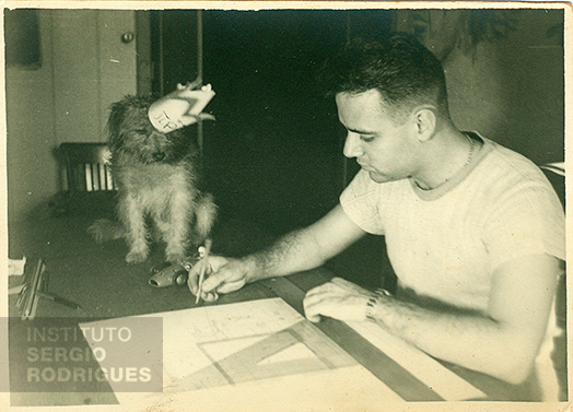 Sergio Rodrigues aos 20 anos de idade, realizando desenho técnico ao lado de sua cadela Pipoca, no Castelinho na Praia do Flamengo, nº 72 – Rio de Janeiro, no ano de 1947.