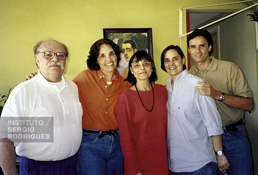 Da esquerda para direita, Sergio Rodrigues ao lado de seus filhos Ângela, Verônica, Adriana e Roberto, em sua residência, no Rio de Janeiro, na década de 2000. Ao fundo, autorretrato de Roberto Rodrigues, pai de Sergio.